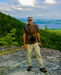 photo of Ken Wells standing on a mountain edge after a hike.