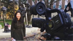 photo shows Sojin giving a report in front of a camera.